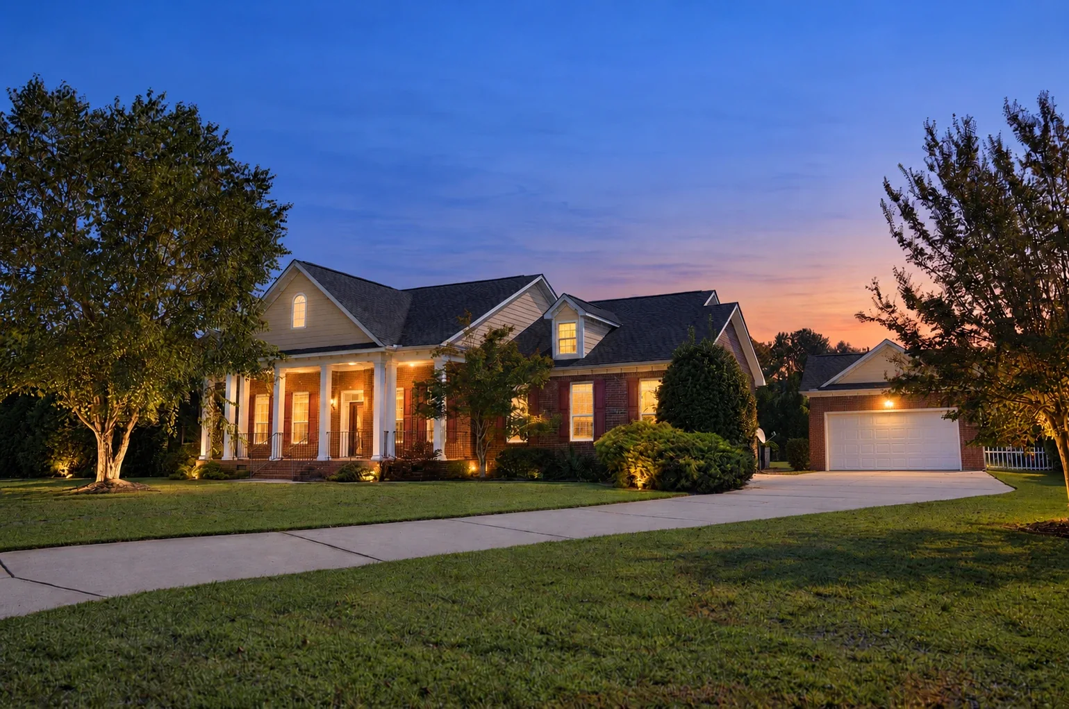 Brick home with a columned front porch, lit at dusk